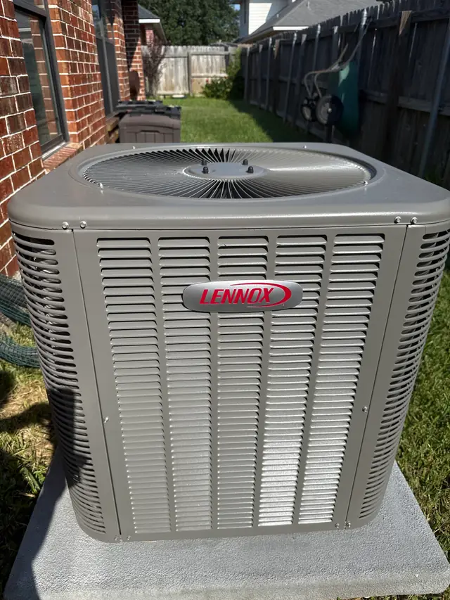 A Lennox condenser set on a fresh pad beside a brick house