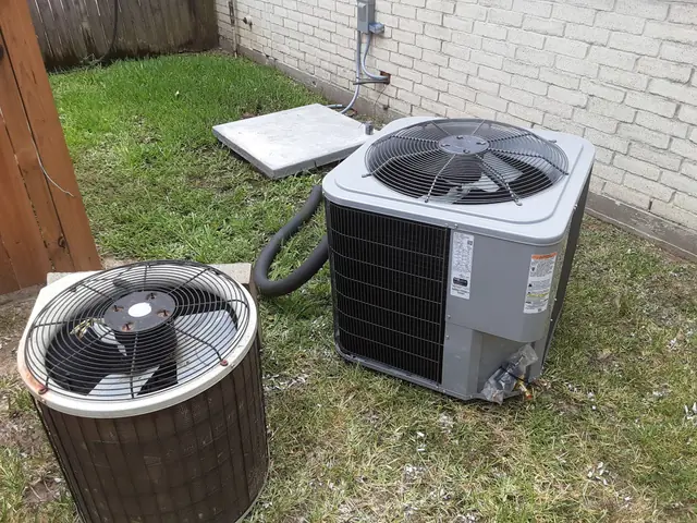 A rusted condenser pulled out on the grass beside the newly set replacement